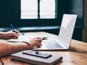 Person writing notes and using laptop